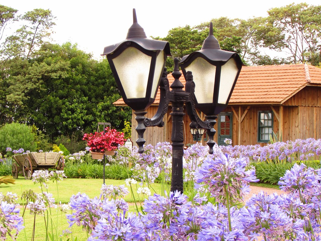 Jardim com lampião e flores roxas diante de casa colonial